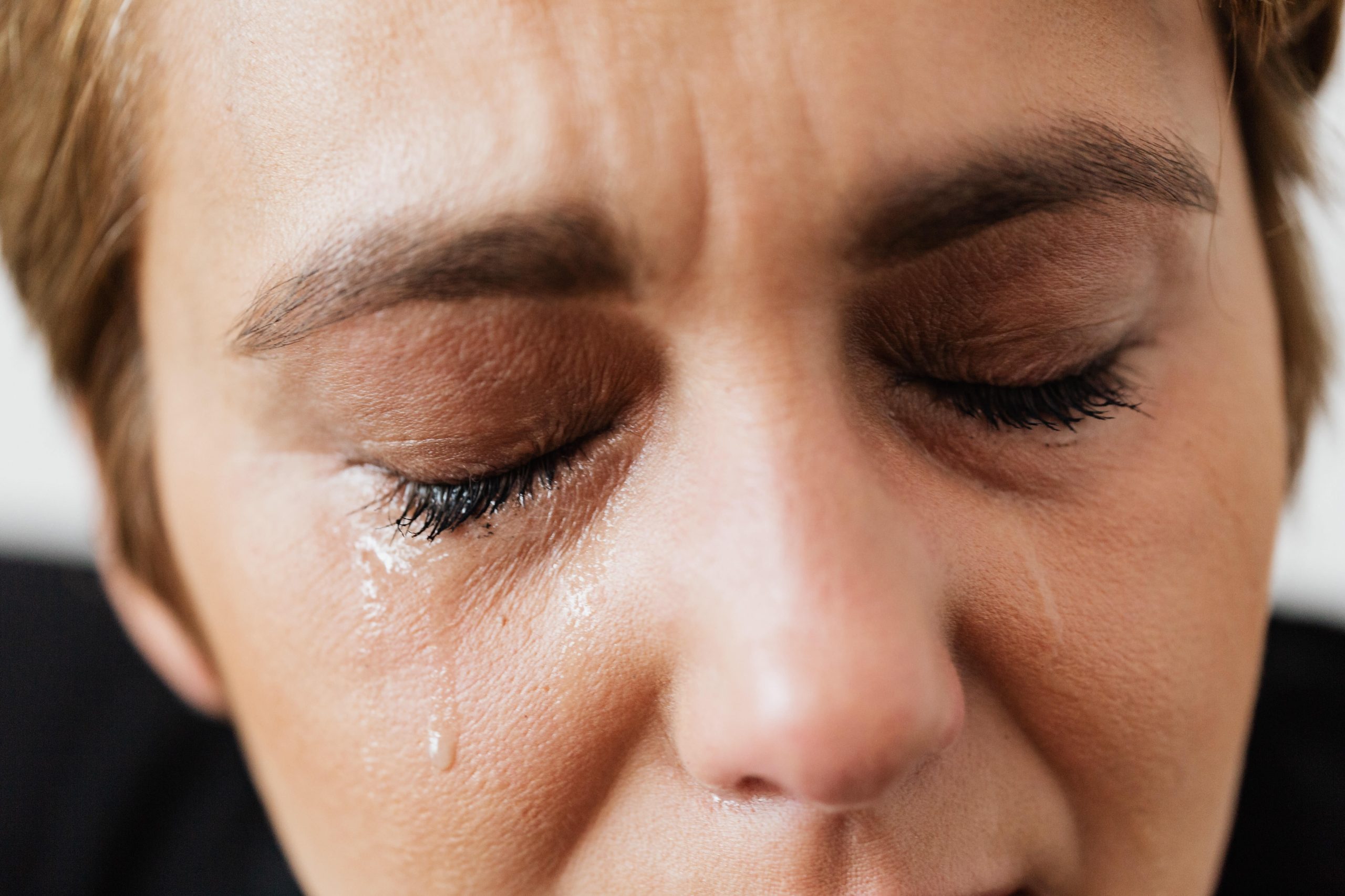 a woman closes her eyes with tear tracks running down her face.